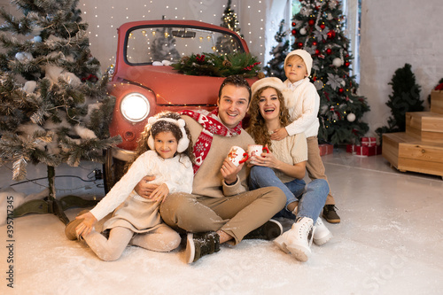 Family Christmas. Cheerful parents and their cute daughter and son waiting for Christmas near red car
