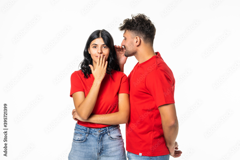 Naklejka premium Portrait of an astonished young couple telling secrets standing together over white background