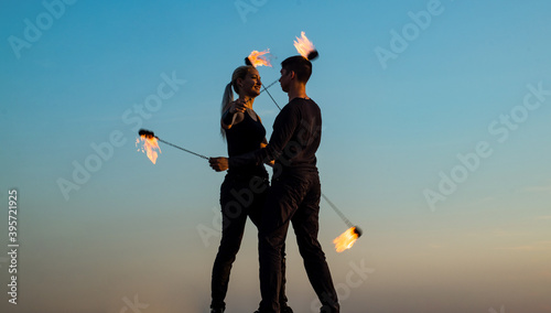 Sexy couple in love dance while spinning burning poi blue sky outdoors, fire show photo