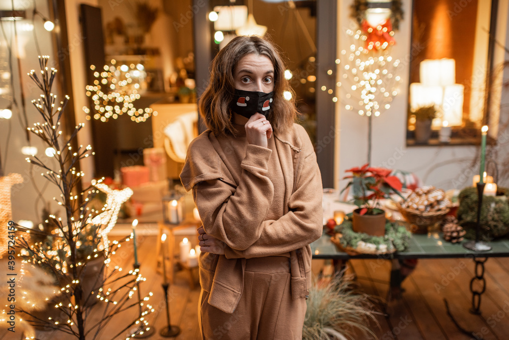 Portrait of a sad woman in facial mask during the New Year holidays at home on the beautifully decorated terrace. Concept of quarantine and self-isolation during the epidemic on holidays