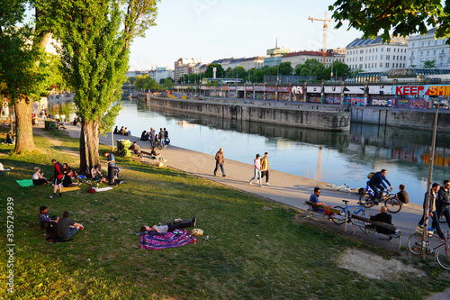 An einem Frühlingstag spazieren die Leute entlang dem sonnigen Donaukanal und die Menschen liegen im Gras und machen Picknick in der Stadt