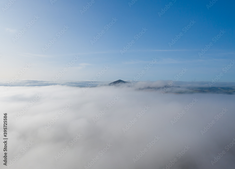 Mountain sitting above the clouds with blue skies and thick fog