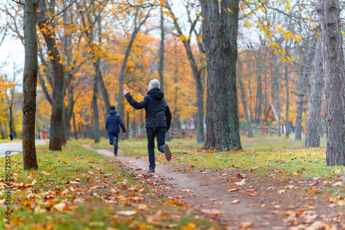 teen girl and boy running through the park and enjoys autumn, beautiful nature with yellow leaves