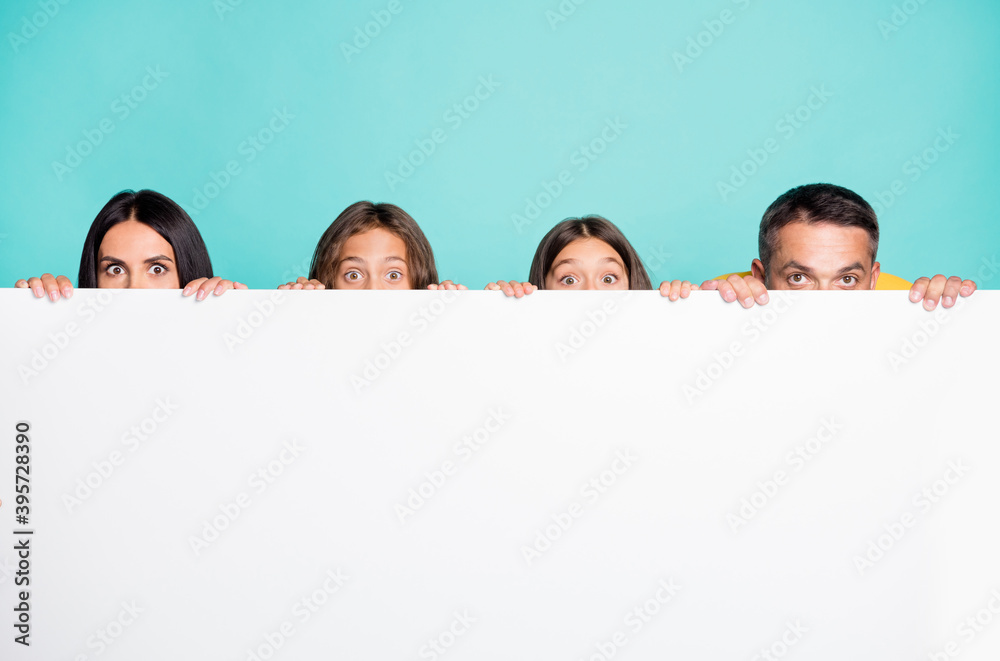 Photo portrait of full family with small kids hiding over white wall isolated on vivid turquoise colored background Photo portrait of full family with small kids hiding over white wall isolated on vivid turquoise colored background