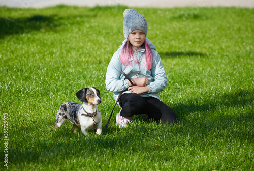 Girl child playing with dachshund dog in autumn sunny park
