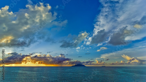 Colorful sunset landscape in the Indian ocean. The horizon is painted in yellow-orange colors, turquoise water, blue sky with white clouds.