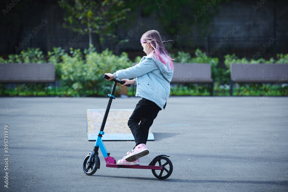 Smiling little girl rides scooter in park. Empty space for text Smiling little girl rides scooter in park. Empty space for text
