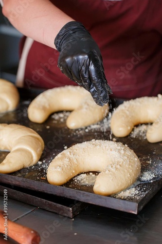 a woman's gloved hand sprinkles bagels in a bakery