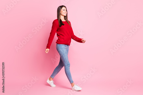 Full length profile photo of lovely girl walk wear red pullover denim jeans sneakers isolated pink color background