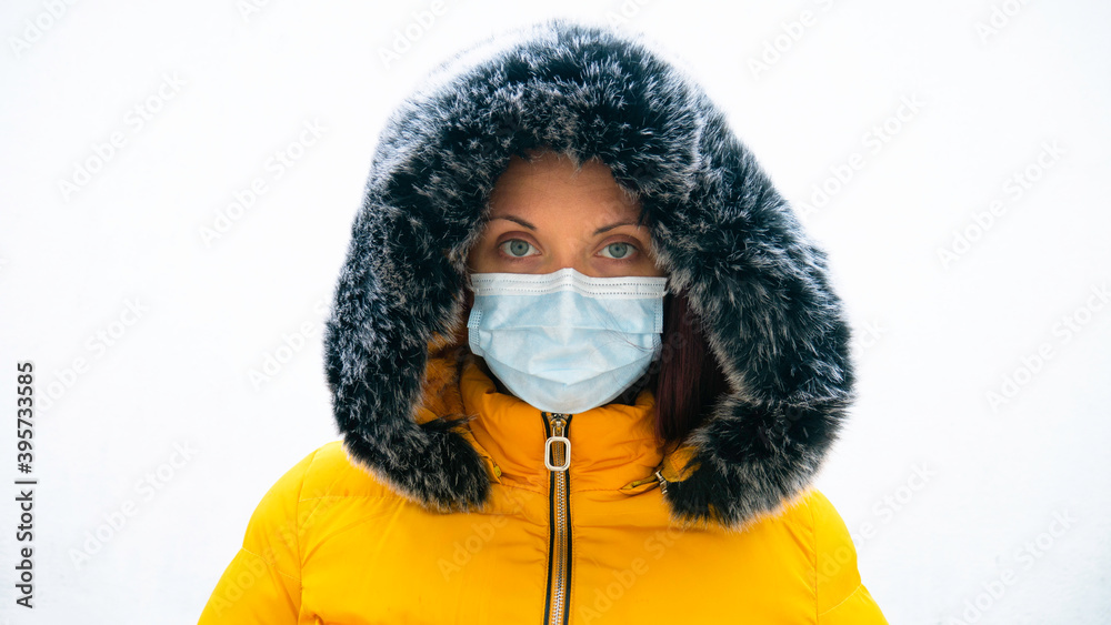 Portrait of a woman in a yellow jacket with a fur hood and a medical mask over her face. Polluted air concept. Portrait of a woman in a yellow jacket with a fur hood and a medical mask over her face. Polluted air concept.