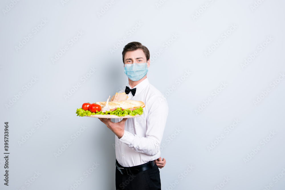 Portrait of classy guy waiter wearing safety gauze mask holding on tray yummy meal serving isolated on gray color background Portrait of classy guy waiter wearing safety gauze mask holding on tray yummy meal serving isolated on gray color background