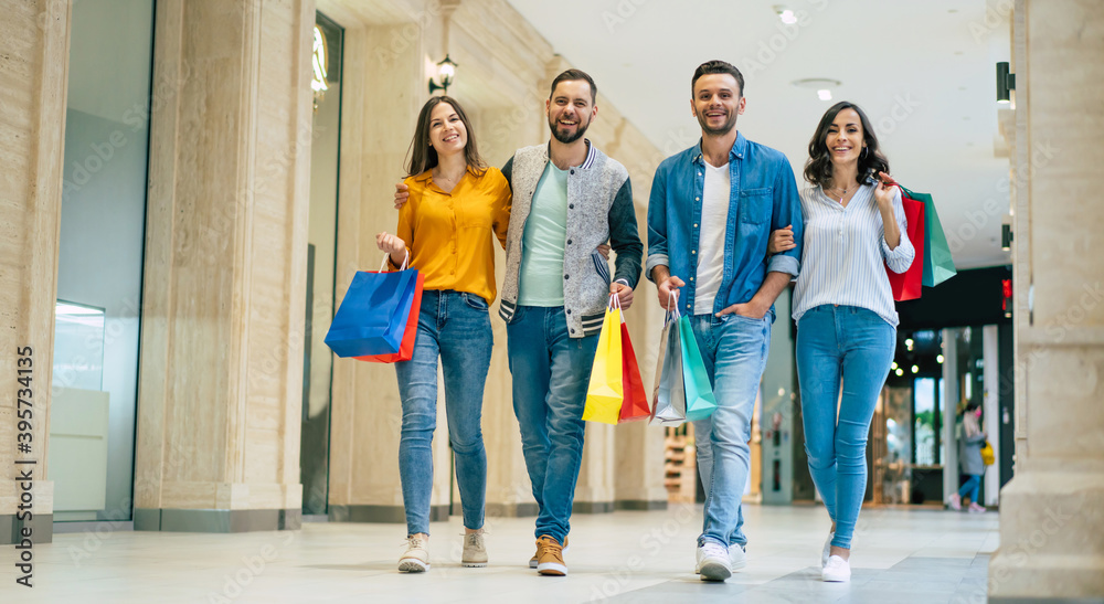 Obraz premium Happy group of excited beautiful modern stylish friends in casual wear with paper bags are walking in the mall during shopping.