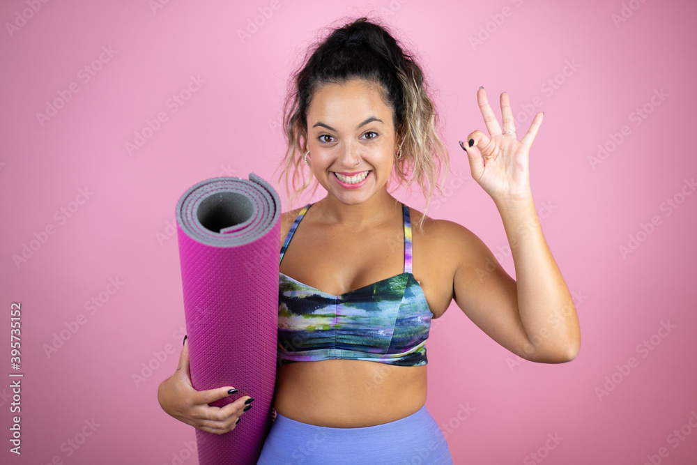 Young beautiful woman wearing sportswear and holding a splinter over isolated pink background doing ok sign with fingers and smiling, excellent symbol