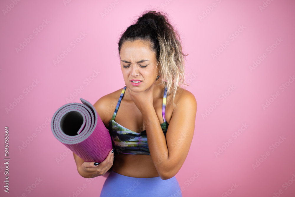Young beautiful woman wearing sportswear and holding a splinter over isolated pink background touching painful neck, sore throat for flu, clod and infection Young beautiful woman wearing sportswear and holding a splinter over isolated pink background touching painful neck, sore throat for flu, clod and infection