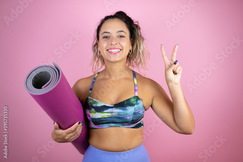 Young beautiful woman wearing sportswear and holding a splinter over isolated pink background showing and pointing up with fingers number two while smiling confident and happy