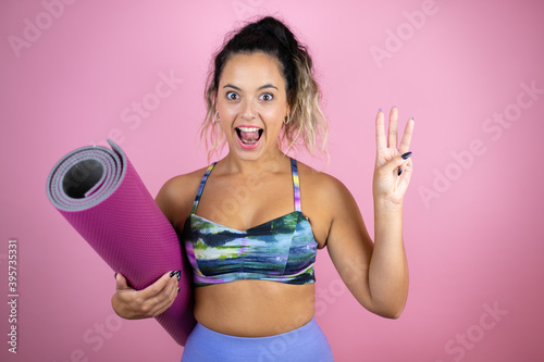 Young beautiful woman wearing sportswear and holding a splinter over isolated pink background showing and pointing up with fingers number three while smiling confident and happy