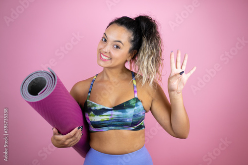 Young beautiful woman wearing sportswear and holding a splinter over isolated pink background showing and pointing up with fingers number four while smiling confident and happy