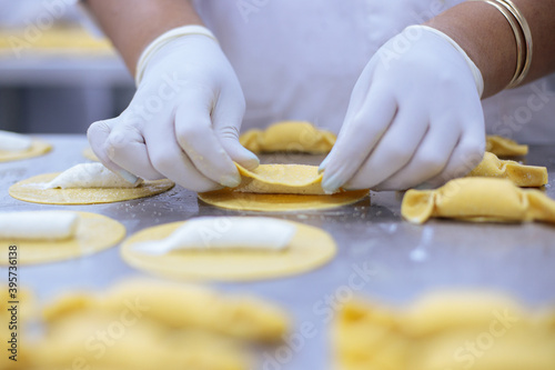 Handmade pasta preparation - woman’s hands, with nylon gloves on, creating a candy shape from pasta with a cheese stuffing.