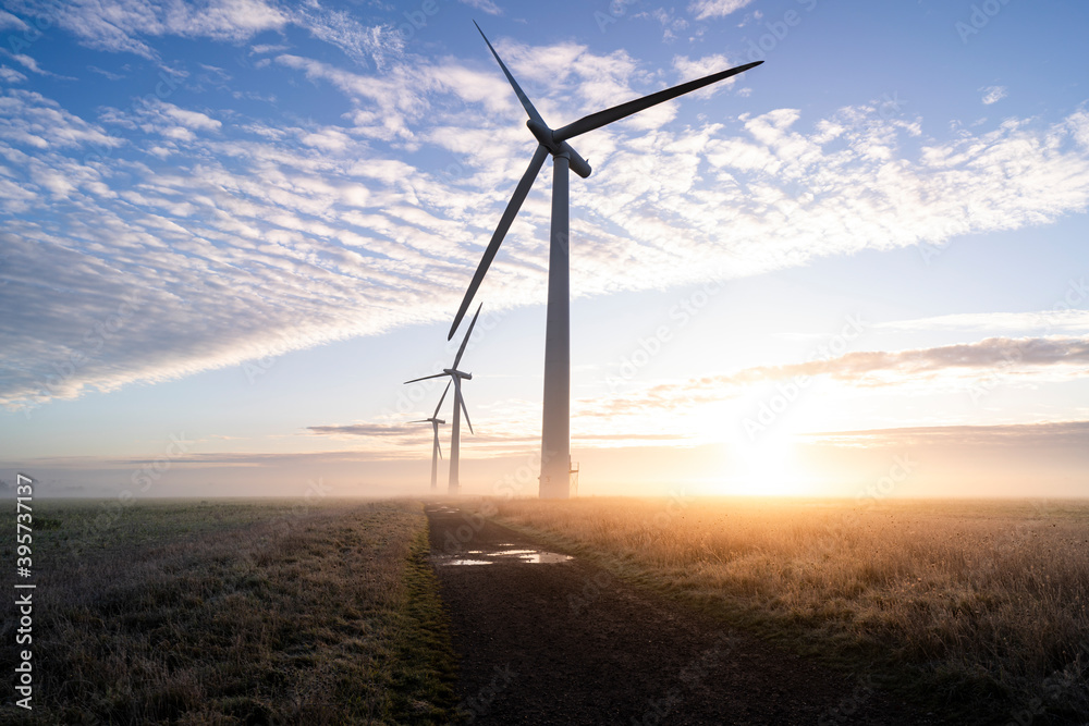 Three commercial wind turbines in thick fog at sunrise in the English countryside casting long shadows