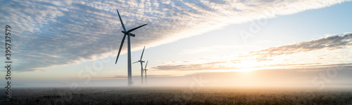 Three commercial wind turbines in thick fog at sunrise in the English countryside panoramic