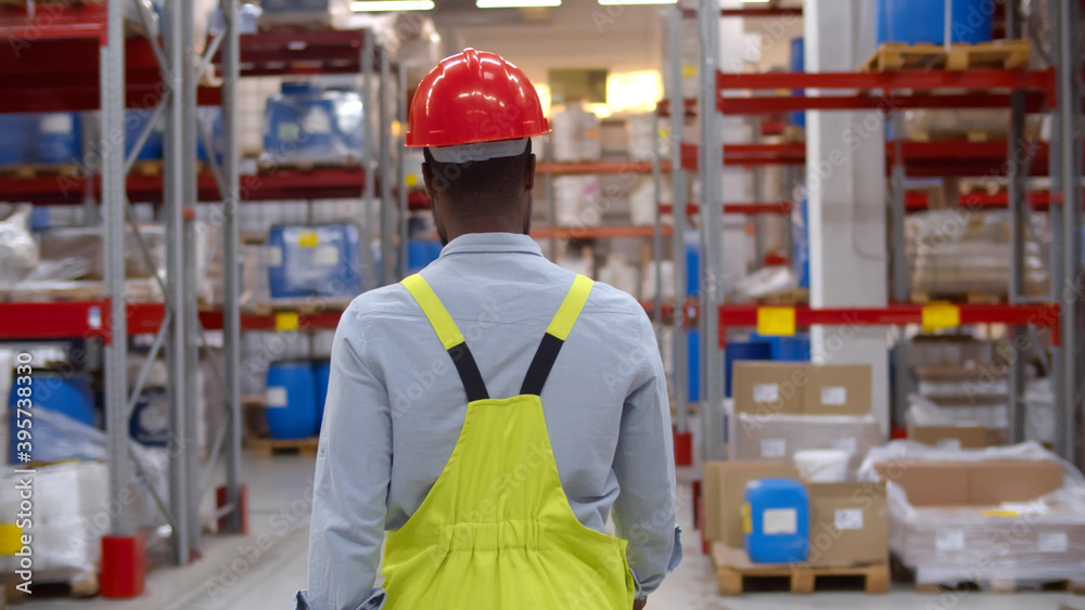 Back view of african worker walking in large warehouse distribution center Back view of african worker walking in large warehouse distribution center