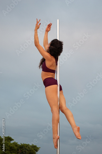 Young Middle Eastern pole dancer, holding a pose on a pole set in an urban park.