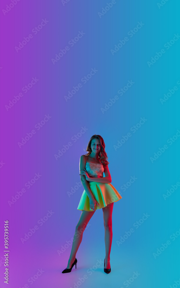 Model posing. Beautiful seductive girl in fashionable yellow skirt on gradient pink-blue neon background. Full-length portrait. Copyspace for ad. Flyer design. Summer, fashion, emotions concept.