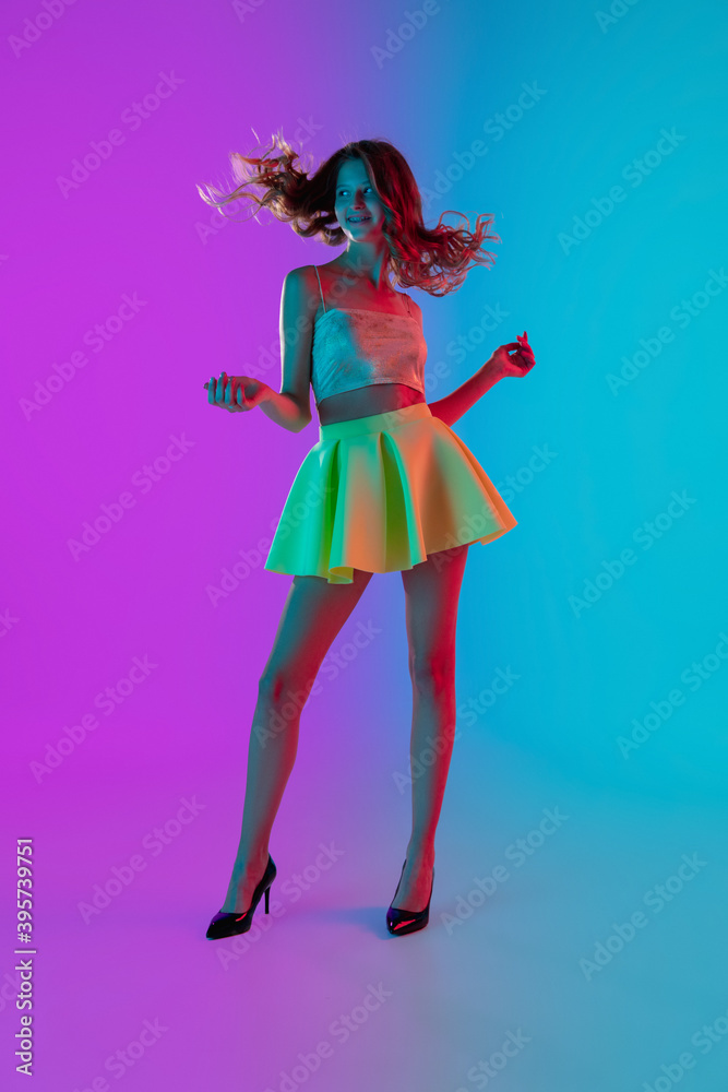 Fototapeta Flowing hair. Beautiful seductive girl in fashionable yellow skirt on gradient pink-blue neon background. Full-length portrait. Copyspace for ad. Flyer design. Summer, fashion, emotions concept.