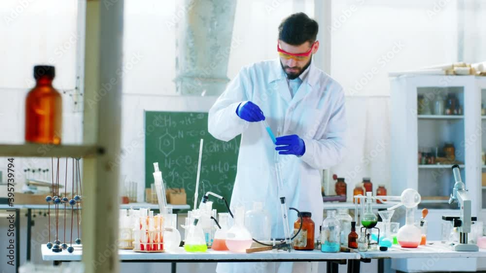 Scientist man in the chemical laboratory using some blue liquid on the glass tub to make a chemical reaction he wearing protective equipment. Shot on ARRI Alexa Mini. Scientist man in the chemical laboratory using some blue liquid on the glass tub to make a chemical reaction he wearing protective equipment. Shot on ARRI Alexa Mini.