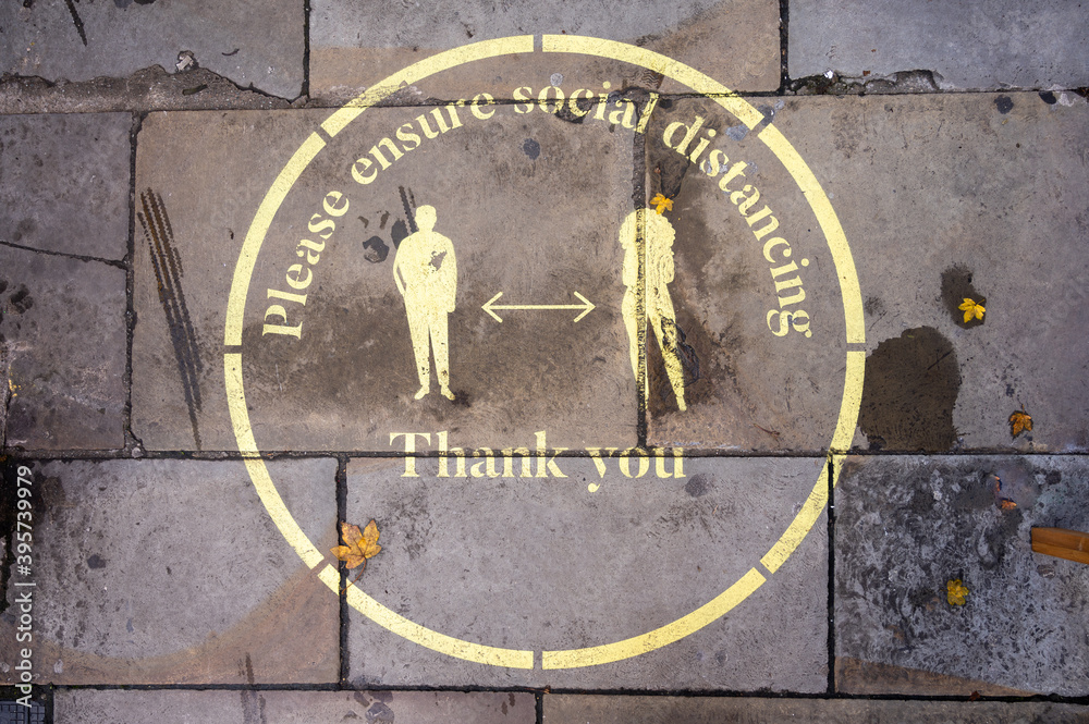 An overhead shot of a yellow Covid 19 social distancing sign painted on the sidewalk in Covent Garden