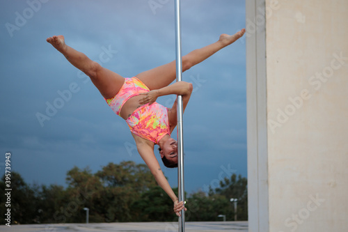 Young Middle Eastern pole dancer, holding a pose on a pole set in an urban park.