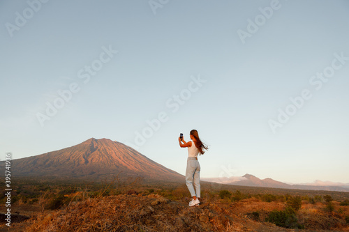 A woman looks at a mountain, a volcano and taking picture on the phone. Rear view. Bali. Agung.