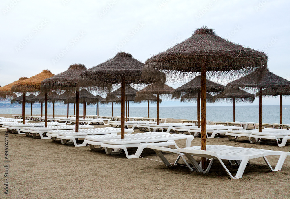 Costa del sol beach in the cloudy weather, end of season. Empty sunbeds and straw umbrellas. 