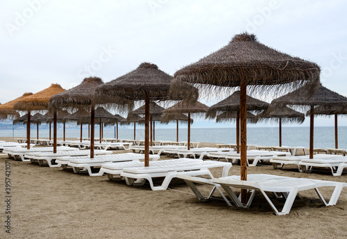 Costa del sol beach in the cloudy weather  end of season. Empty sunbeds and straw umbrellas. 