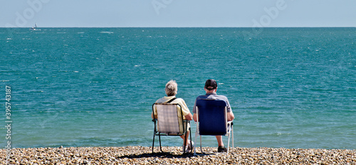 Couple sitting in chairs on a shinge beach looking out to sea.