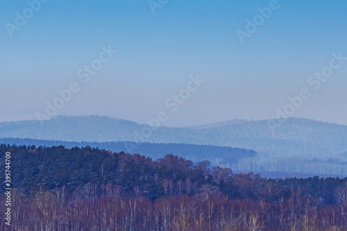 Winter view of forested hills against a blue sky with white clouds