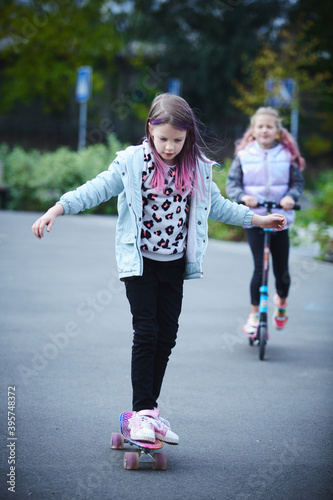 Two pretty little sisters having fun together learning to skateboard outdoors. The concept of a healthy lifestyle. Kids sport