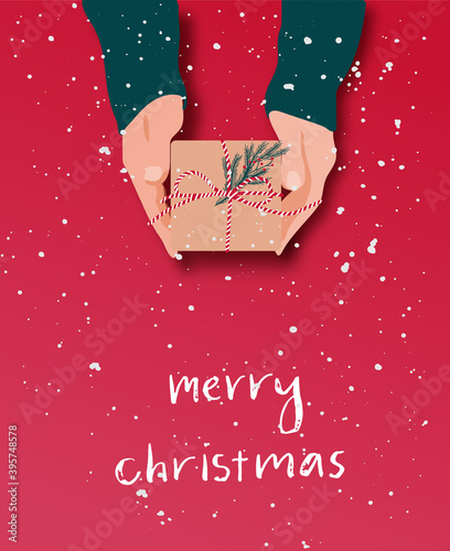 Female's hands in pullover holding Christmas gift box decorated with evergreen branch on red background with snow. Christmas and New Year banner.