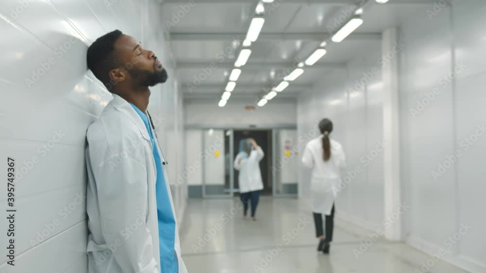 Tired male african doctor standing in hospital corridor Tired male african doctor standing in hospital corridor