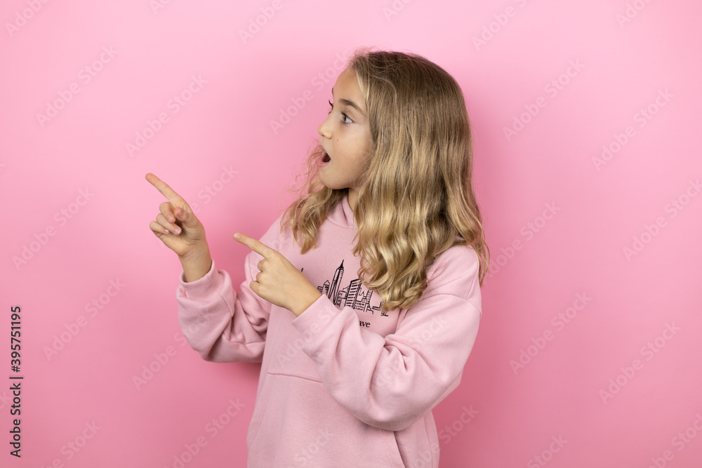 Young beautiful child girl standing over isolated pink background surprised, looking and pointing side Young beautiful child girl standing over isolated pink background surprised, looking and pointing side