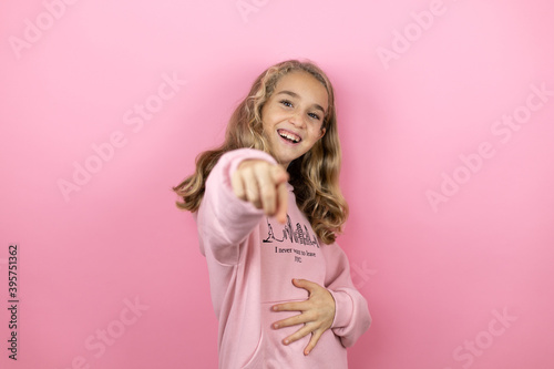 Young beautiful child girl standing over isolated pink background laughing at you, pointing finger to the camera with hand over body, shame expression