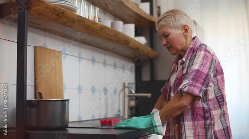 Tired mature woman cleaning cooking top in kitchen