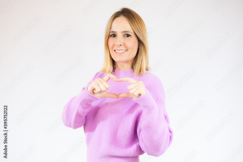 Portrait of young, pretty woman in casual sweater showing with her finger heart figure, sending love to her lover, standing over white background Portrait of young, pretty woman in casual sweater showing with her finger heart figure, sending love to her lover, standing over white background