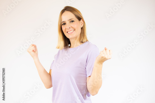 Photo of cheerful beautiful young woman standing isolated over white wall background. Looking camera showing winner gesture. © Danko