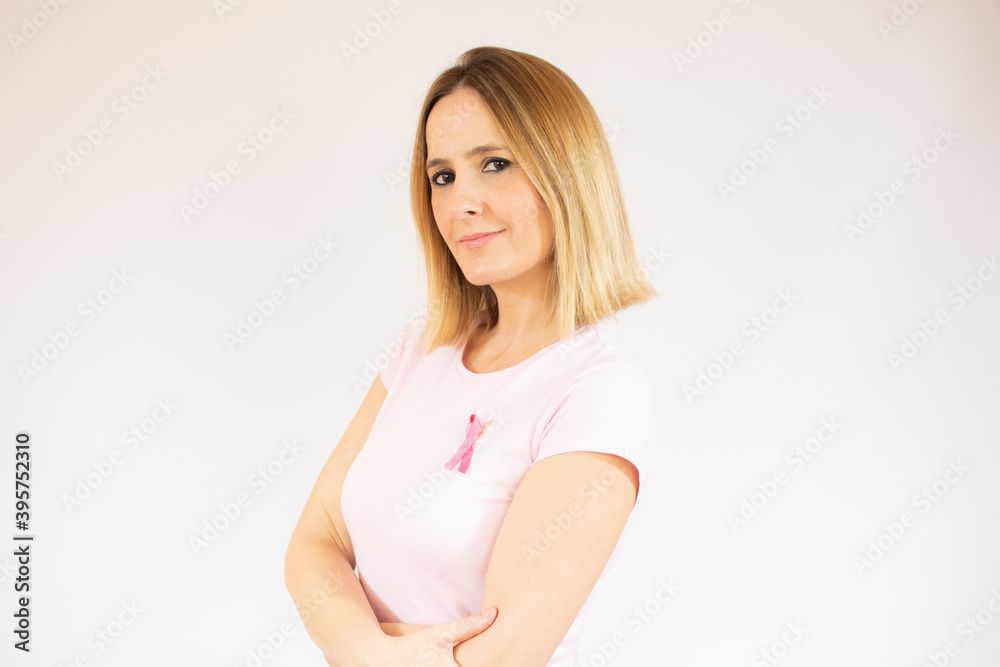 Women against breast cancer. Beautiful woman wearing casual t-shirt with a pink ribbon on her chest and smiling, on white background Women against breast cancer. Beautiful woman wearing casual t-shirt with a pink ribbon on her chest and smiling, on white background