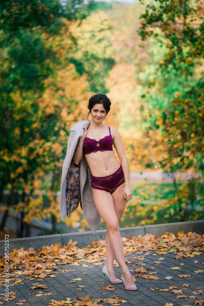 Young beautiful dark-haired woman with slender figure in lingerie and classic coat in autumn park Young beautiful dark-haired woman with slender figure in lingerie and classic coat in autumn park