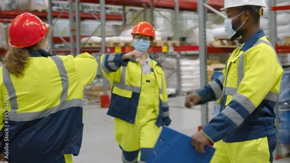 Diverse warehouse workers in face mask do elbow bump greeting
