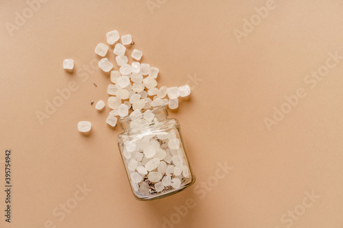 фотографія Raw lumps of sugar mixed with lavender fall out of a glass jar on a beige backgr