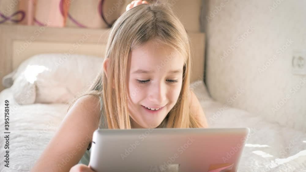 Teenage girl in bed playing a tablet in social internet. Girl watching funny video on the digital tablet.