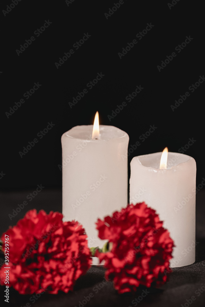 red carnation flowers and candles on black , funeral concept red carnation flowers and candles on black , funeral concept